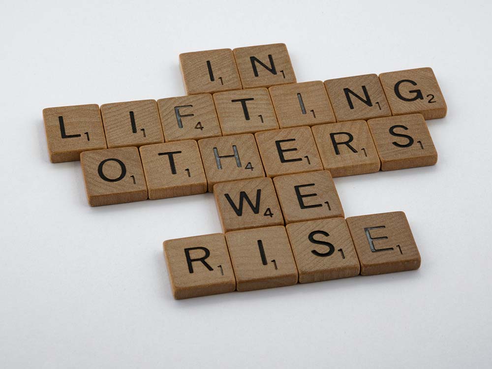 square tiles made of thin wood with one letter on each tile spelling out the phrase "In lifting others we rise"
